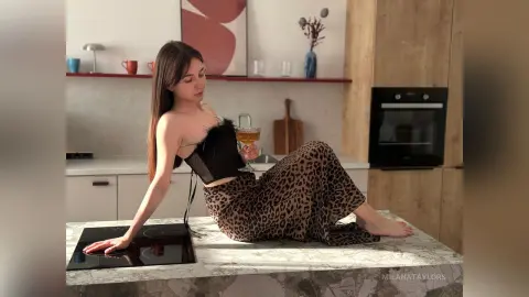 Young woman in a black corset and leopard print skirt sitting on a marble kitchen counter holding a glass of wine.