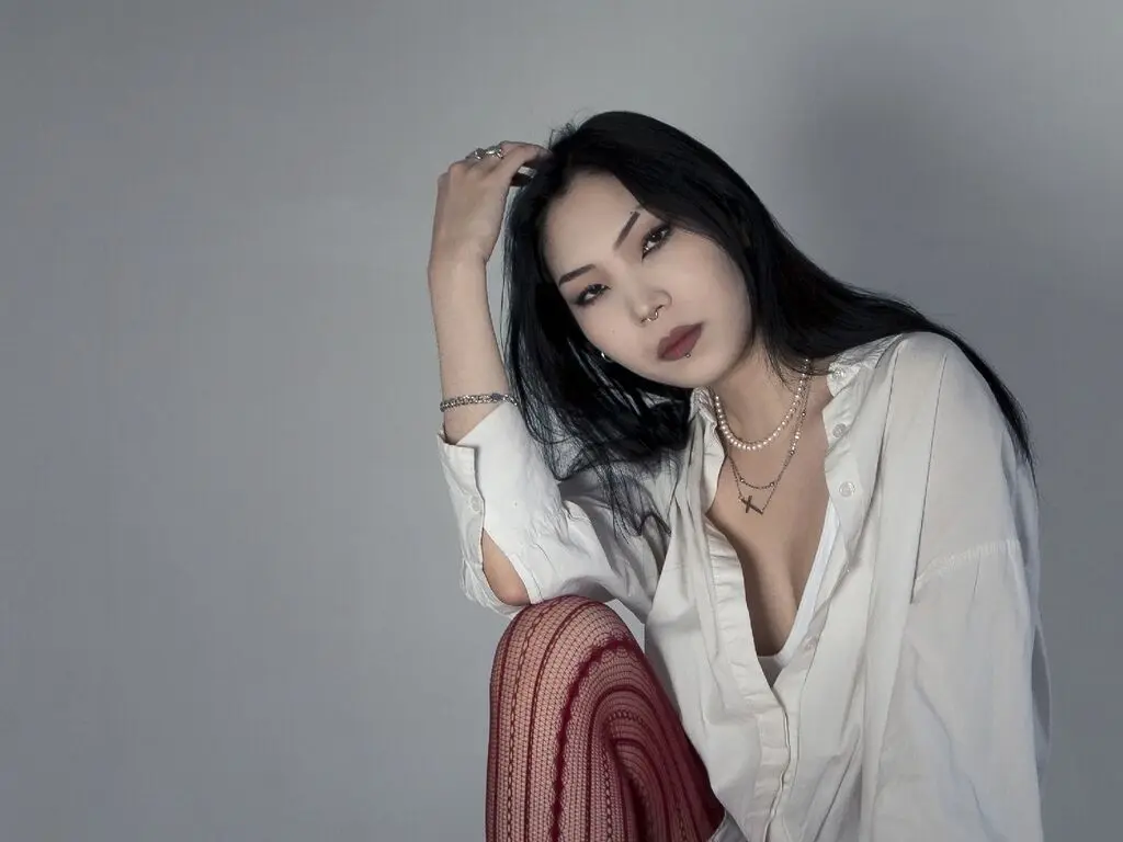 Elegant woman with long black hair in a white button-down shirt posing against a grey studio background.