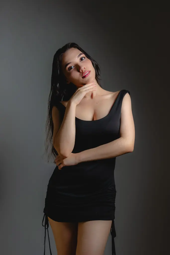 RoouseVega poses in a silver metallic corset top, letting her long dark hair fall over her shoulders against a plain tan background.