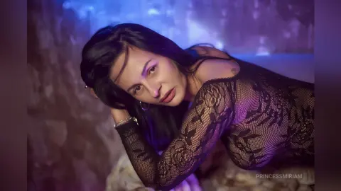 Woman in black lace long-sleeve top posing in moody purple lighting.