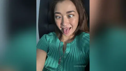Playful young woman in a green ribbed top making a funny face while sitting in a black chair.