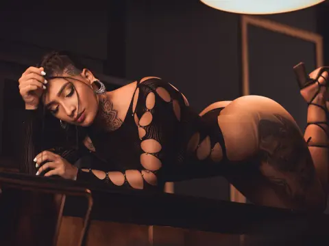 Curvy woman in a black cutout bodysuit lounging on a dark table in a moody, cinematic setting.