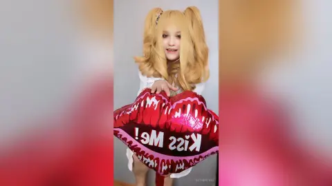 EstherTrix smiles while holding a large red heart-shaped balloon that says Kiss Me!