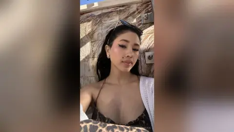 Young woman in a leopard print bikini and white cardigan posing outdoors in sunny lighting.
