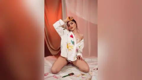 Young woman in a white oversized shirt sitting on a bed in a warm, dreamy indoor setting.