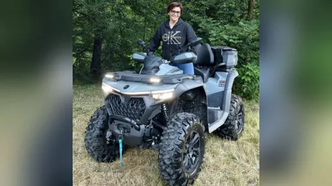 JaneHope — JaneHope smiles while sitting on a grey ATV in a grassy field surrounded by trees.