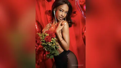 Glamorous woman in black lingerie holding a red rose bouquet against a romantic red backdrop.