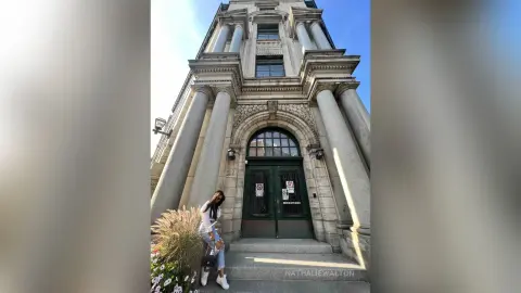 Stylish woman in a white top and jeans standing before a grand classical building with stone columns.