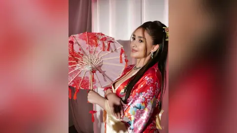 Elegant woman in red floral kimono holding a traditional paper parasol in a soft, romantic studio setting.