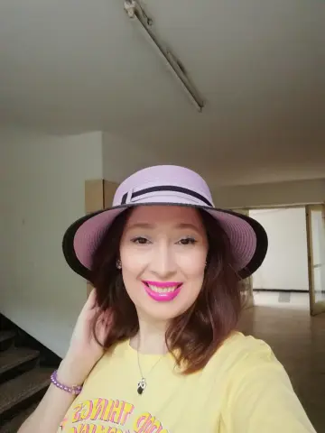 Smiling woman in a pink sun hat and yellow graphic t-shirt posing indoors with a cheerful mood.