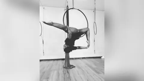 KeianHoz arches her back while hanging upside down from an aerial hoop in a studio setting.