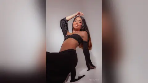 Smiling young woman in a chic black crop top and long skirt posing against a minimalist white background.