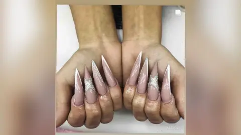 Elegant long stiletto manicured nails with nude polish and sparkling silver glitter accents on female hands.