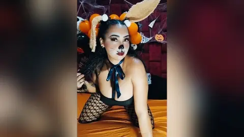 Woman in bunny costume and fishnet tights posing with Halloween decorations and orange balloons.