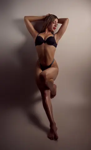Slim woman in black lace lingerie posing confidently against a neutral studio background.