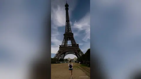 JessicaAidennn — A traveler with a backpack standing before the Eiffel Tower in Paris under a bright blue sky.