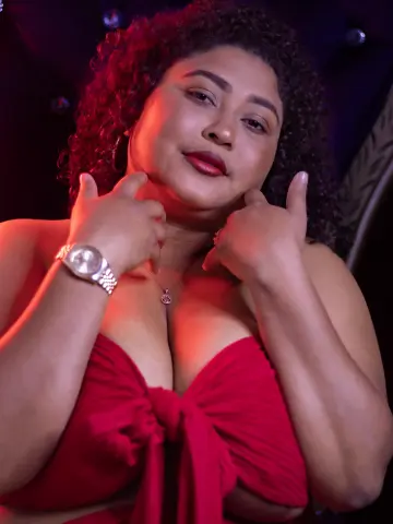 Curvy woman with curly hair in a red strapless top posing confidently in moody, warm lighting.