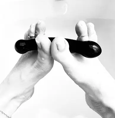 Close-up of hands using a black gua sha facial massage tool for a relaxing skincare routine.