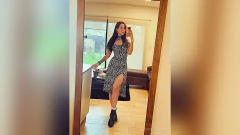 LucyRosenfelds poses in a full-length mirror wearing a black and white patterned dress with a high slit and black boots.