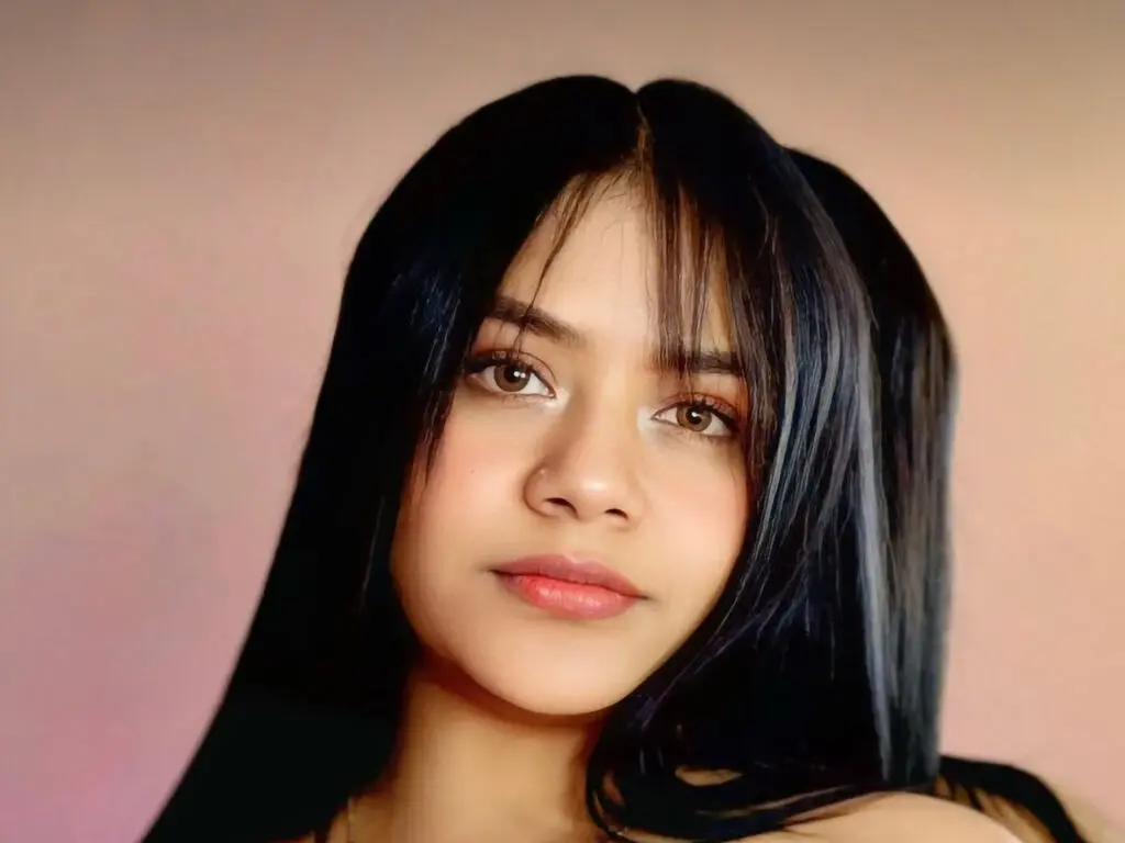 Young woman with long dark hair and natural makeup looking serene against a soft pink background.