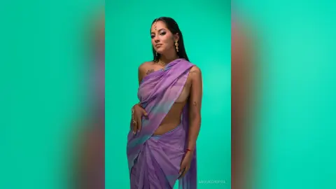Elegant woman in a purple ombre saree posing against a vibrant teal background with a graceful mood.