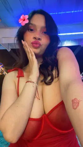 Young woman in a red velvet dress with a pink flower in her hair posing under blue neon lights.
