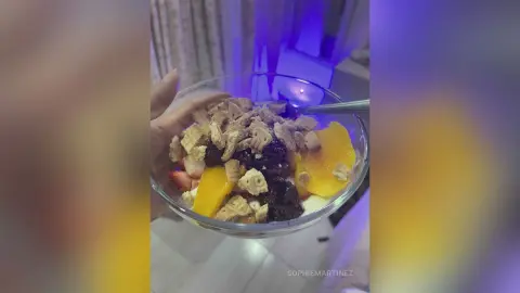 Delicious fruit parfait with granola, berries, and sliced mango served in a glass bowl under soft blue lighting.