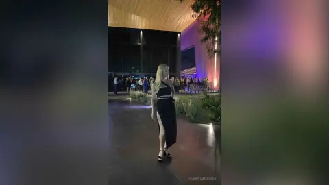Elegant woman in a black evening gown standing on a modern balcony at a glamorous night event.
