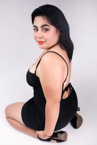 Smiling woman in a black cocktail dress posing against a white background for a chic fashion portrait.