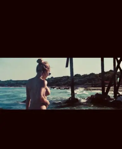 Blonde woman in a bikini enjoying a sunny day by the ocean waves near a wooden pier.