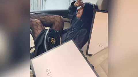 Stylish woman in black outfit and patterned tights relaxing with luxury Gucci shopping bags.