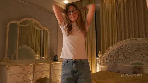 Young woman in a white t-shirt and jeans posing in a cozy, sunlit bedroom with vintage decor.