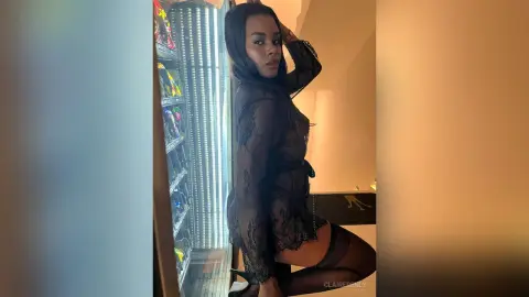 Elegant woman in a black lace sheer outfit posing confidently in a dimly lit modern interior.