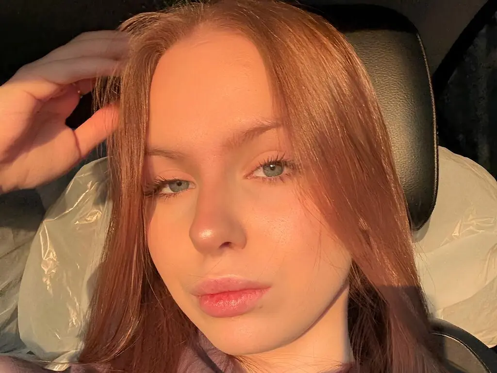 Close-up portrait of a young woman with long reddish hair sitting in a car during golden hour lighting.