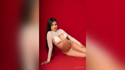 Young woman in a white lace long-sleeve crop top and bikini bottoms posing against a vibrant red background.