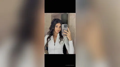 CatherineThomase — CatherineThomase takes a mirror selfie wearing a tight white long-sleeve top and smiling.