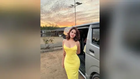 Beautiful woman in a yellow sundress standing by a silver van during a golden hour sunset.