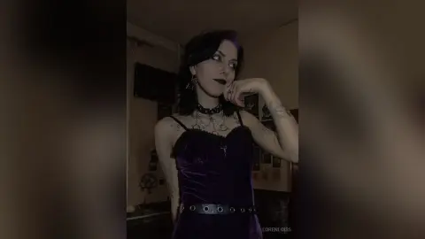 Gothic woman in a dark velvet dress and silver choker posing in a moody, dimly lit room.
