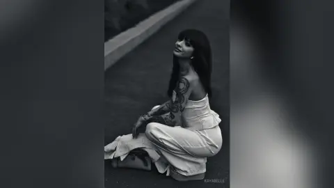 Tattooed woman in a white elegant dress sitting on a street in a moody black and white portrait.