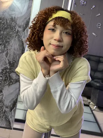 Jessiee_Belle with curly brown hair and a yellow headband poses in a yellow ribbed outfit.