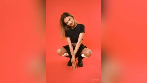 Smiling young woman in a black t-shirt and shorts posing against a vibrant red studio background.