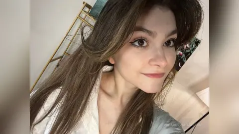 Smiling young woman with long brown hair wearing a white shirt in a bright indoor setting.