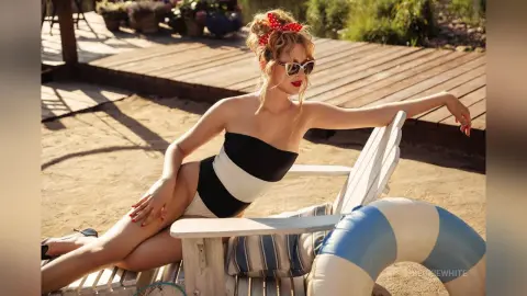 Glamorous woman in a black and white swimsuit relaxing on a white lounge chair at a sunny beach resort.