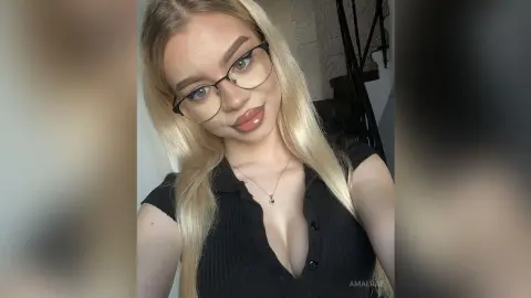 Blonde woman in black ribbed top and glasses smiling in a bright indoor setting.
