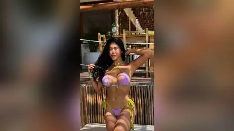 Smiling young woman in a purple bikini relaxing on a sunny tropical wooden deck.