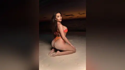 Curvy woman in an orange bikini posing on a sandy beach at twilight under a dark sky.