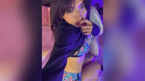 Young woman in a colorful patterned bikini set posing in moody purple lighting at home.
