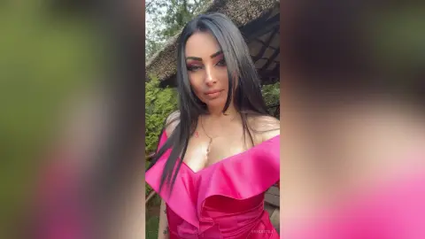 Beautiful woman in a pink off-the-shoulder ruffle dress posing outdoors in a serene garden setting.