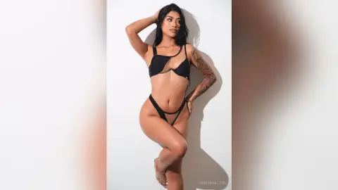 Confident woman in a black bikini posing against a white studio background.
