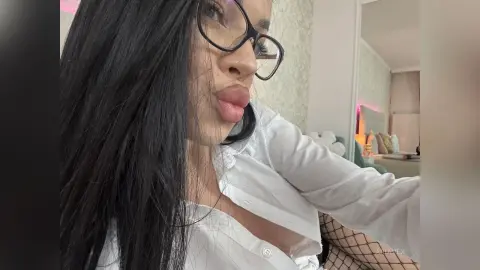 AriaVex wears black glasses and a white button-down shirt while looking toward the camera with long black hair.